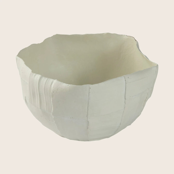 Handcrafted ceramic bowl with irregular edge and textured surface, light-colored.
