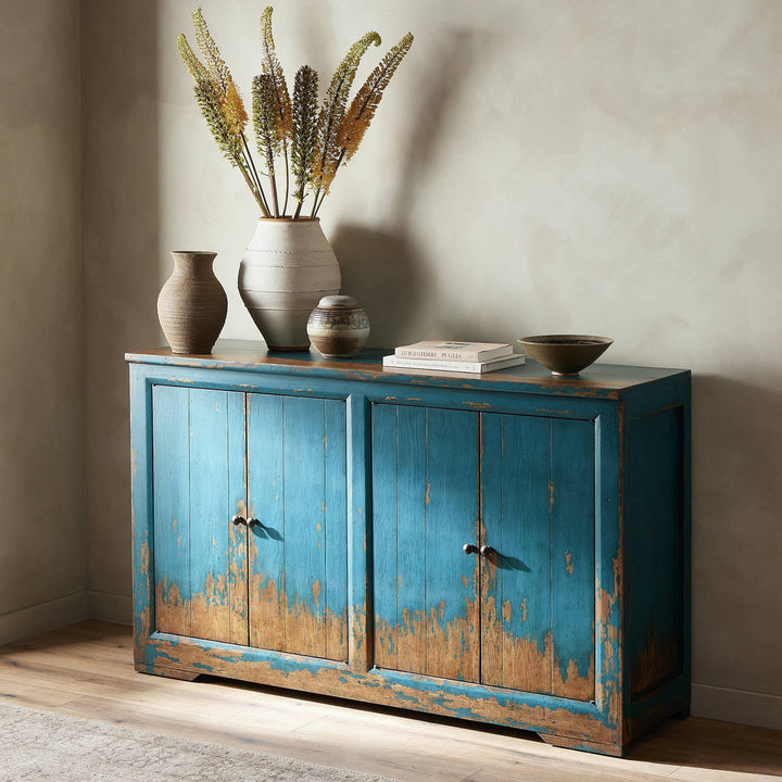 Rustic sideboard with distressed blue finish, adorned with vases and books.
