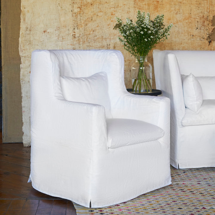 Two white slipcovered armchairs with white flowers in vase.