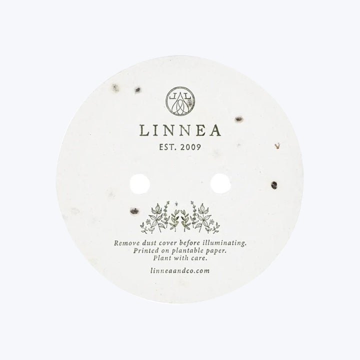 Circular white object with LINNEA EST. 2009 & plantable paper instructions.