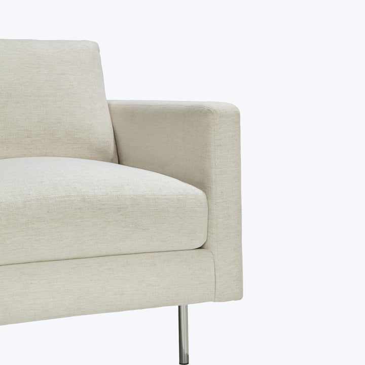 Modern armchair with light beige fabric upholstery and sleek metallic leg.