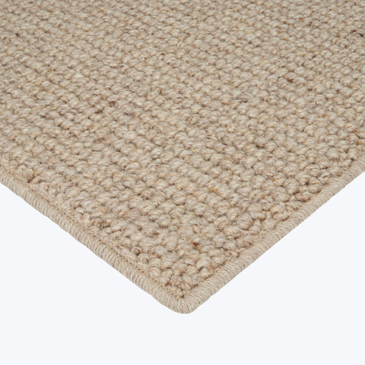 Close-up of dense loop pile beige area rug with bound edges.