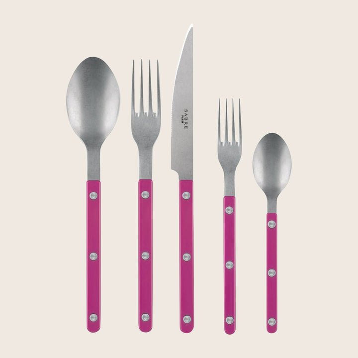 Set of cutlery with pink handles including spoon, fork, knife, and smaller spoon, arranged in a row.