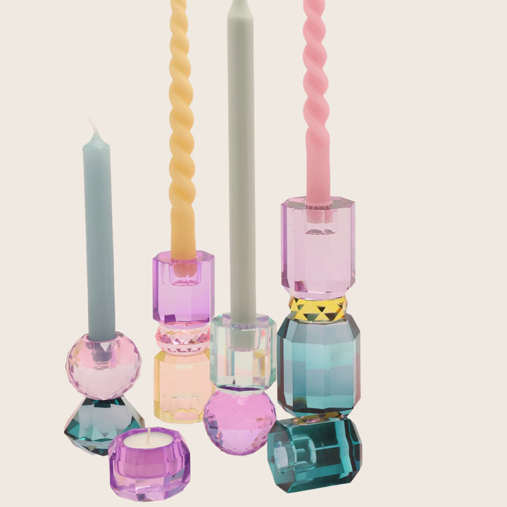 Colorful candles in eclectic holders against soft pink background decor.