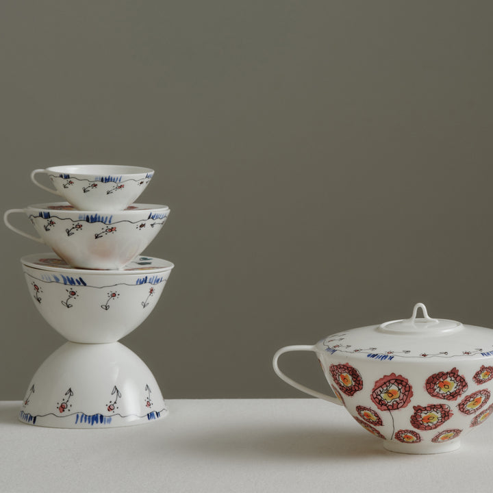 Stacked porcelain tea cups and matching teapot with floral designs.