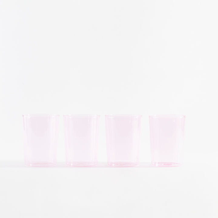 Four empty pink glasses in a row on white background.