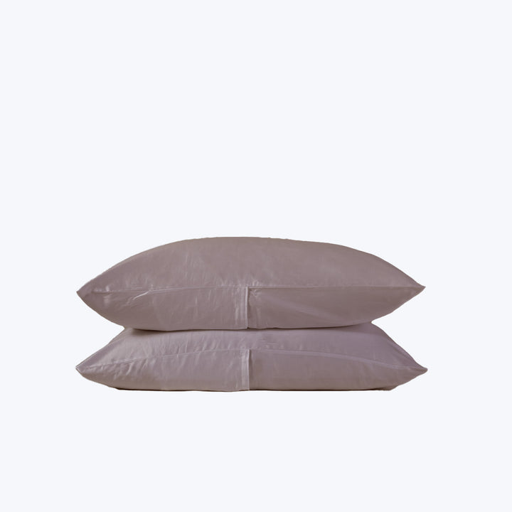Two stacked pillows with soft, wrinkled light-colored pillowcases on white background.