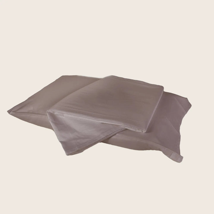 Taupe satin bed sheet and pillowcases set on neutral background.