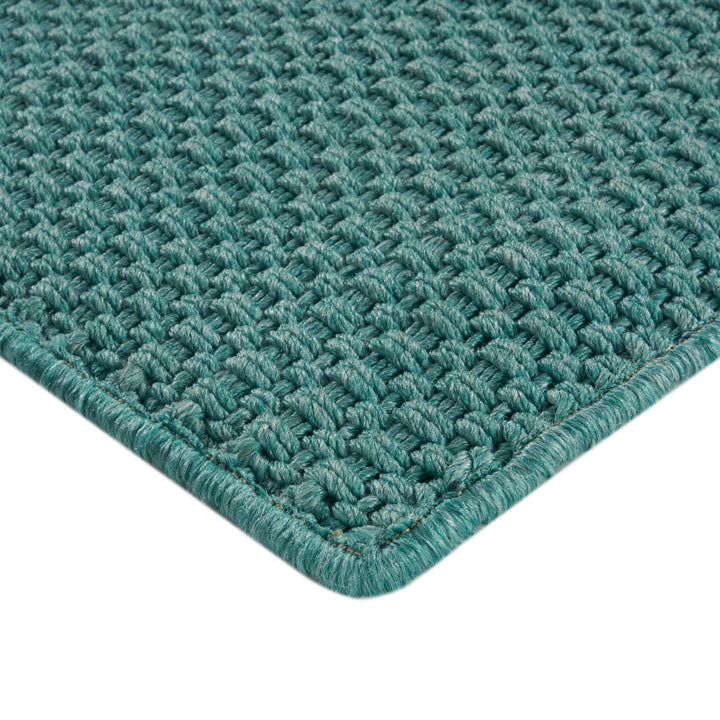 Close-up of teal/green woven rug with intricate loop & knot pattern.