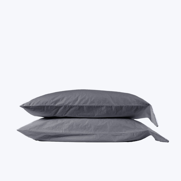 Two stacked rectangular pillows in grey pillowcases on light background.