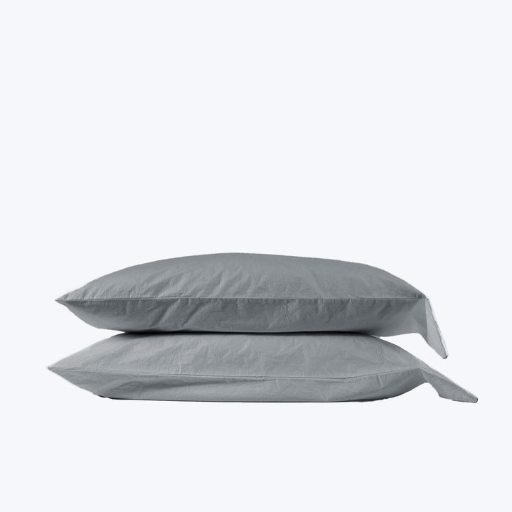 Two stacked gray pillows with pillowcases in light background setting.