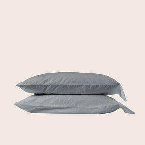 Two stacked gray pillows with pillowcases in light background setting.