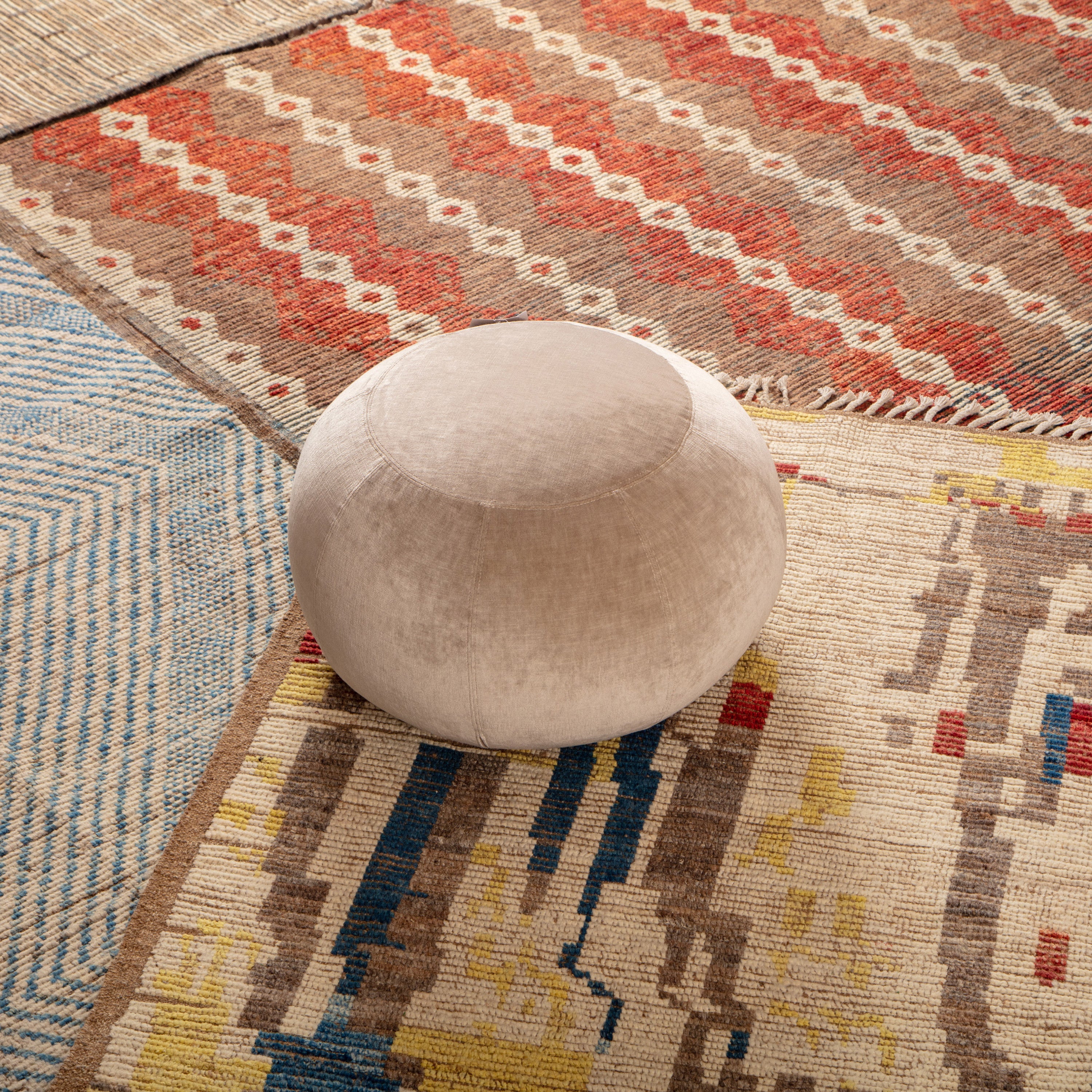 Top-down view of neutral pouf on eclectic patterned rugs.