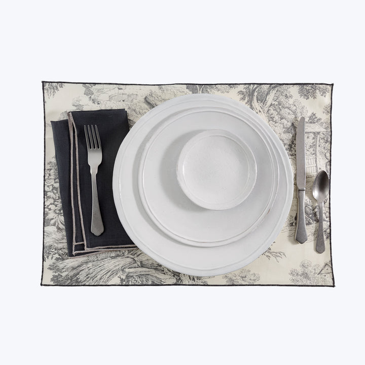 Elegant formal place setting with detailed placemat and metallic flatware.