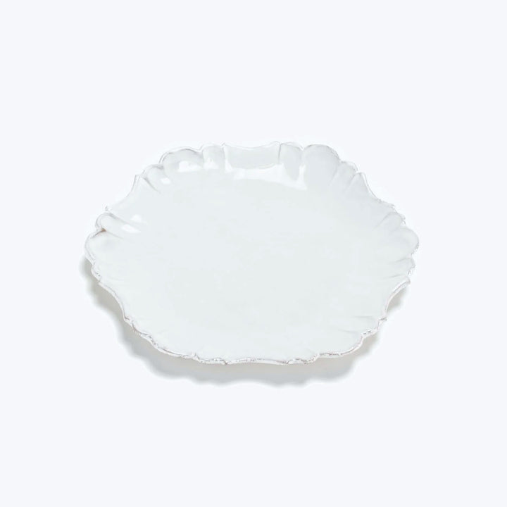 Elegant white scalloped-edge plate on minimalist white background.