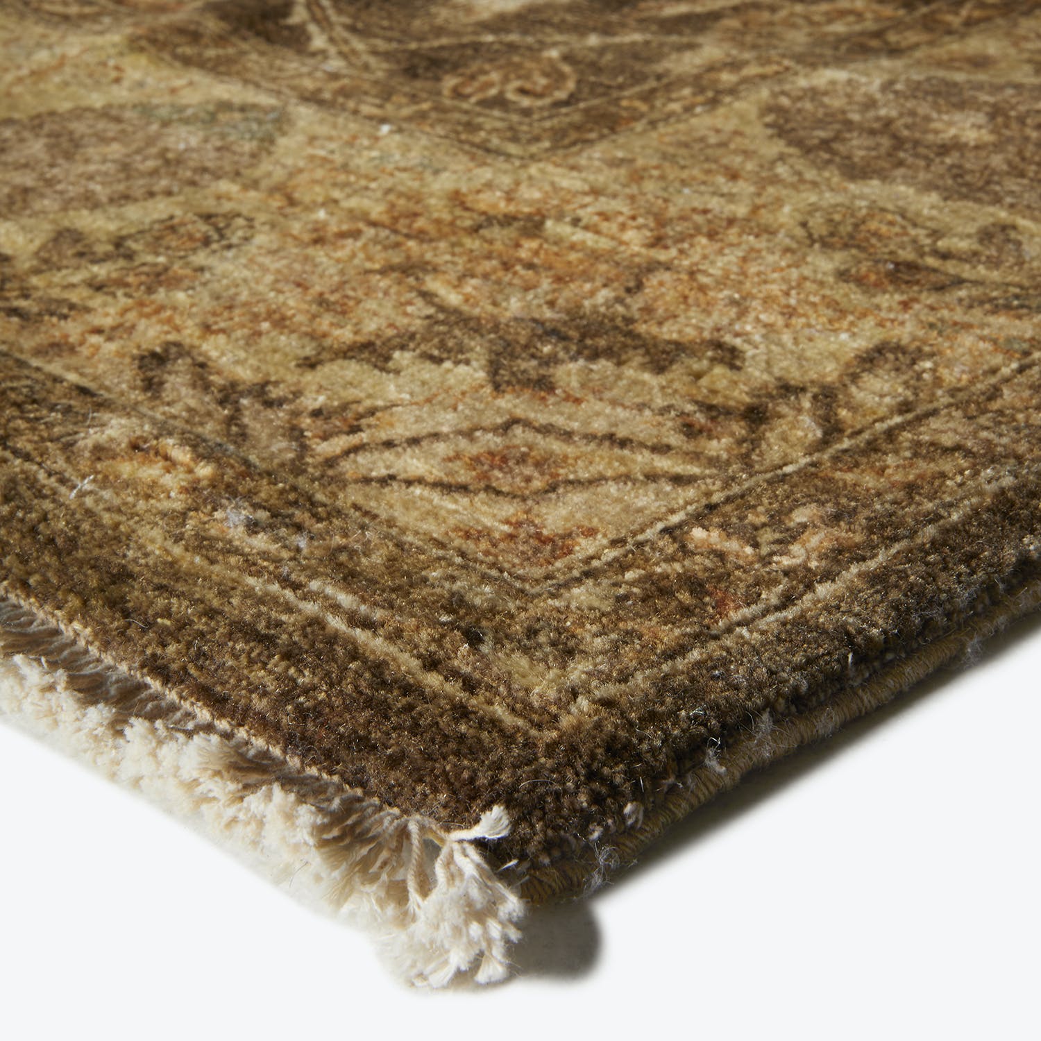 A close-up of a plush, earth-toned, floral-patterned rug with fringe.