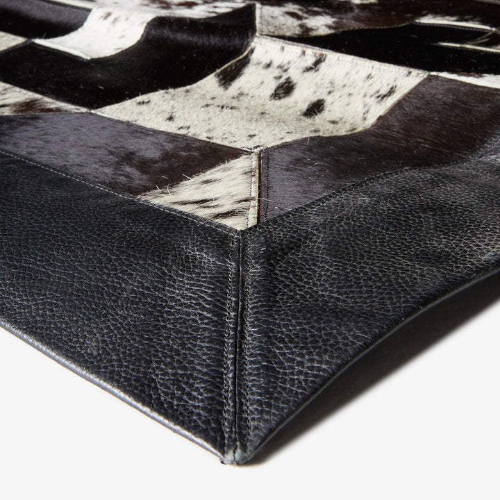 Close-up view of checkered patterned surface with black leather and cowhide materials, suggesting upholstery craftsmanship in furniture or accessories.