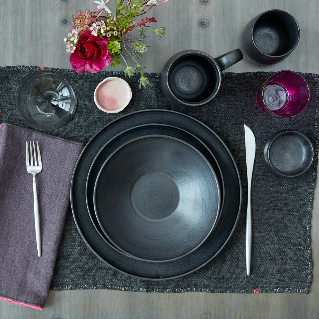 Top-down view of a modern table setting with dark dishware, colorful flowers, and a minimalist aesthetic.