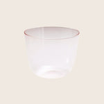 Translucent glass tumbler with a subtle red rim on white background.