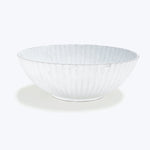 White ceramic bowl with fluted design and rustic, handmade look.
