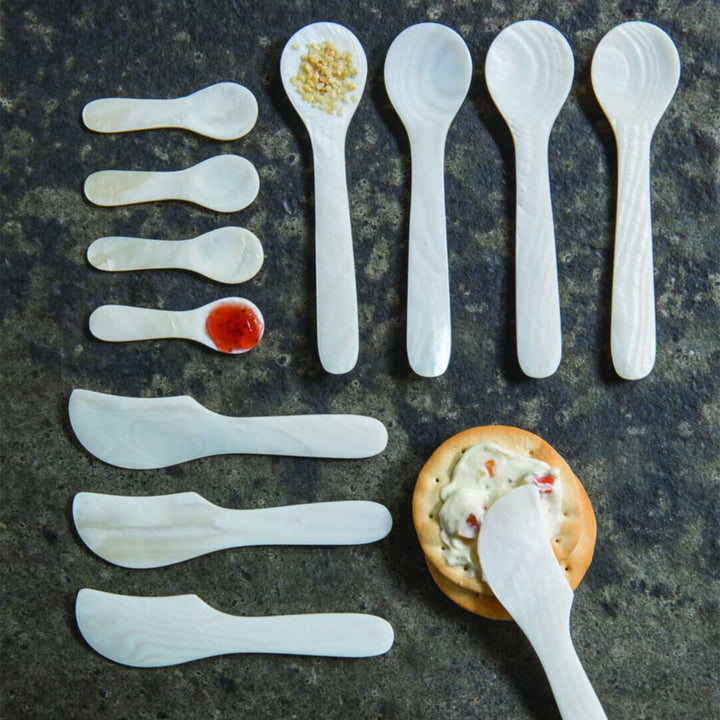 Assortment of white spoons with food on dark surface.