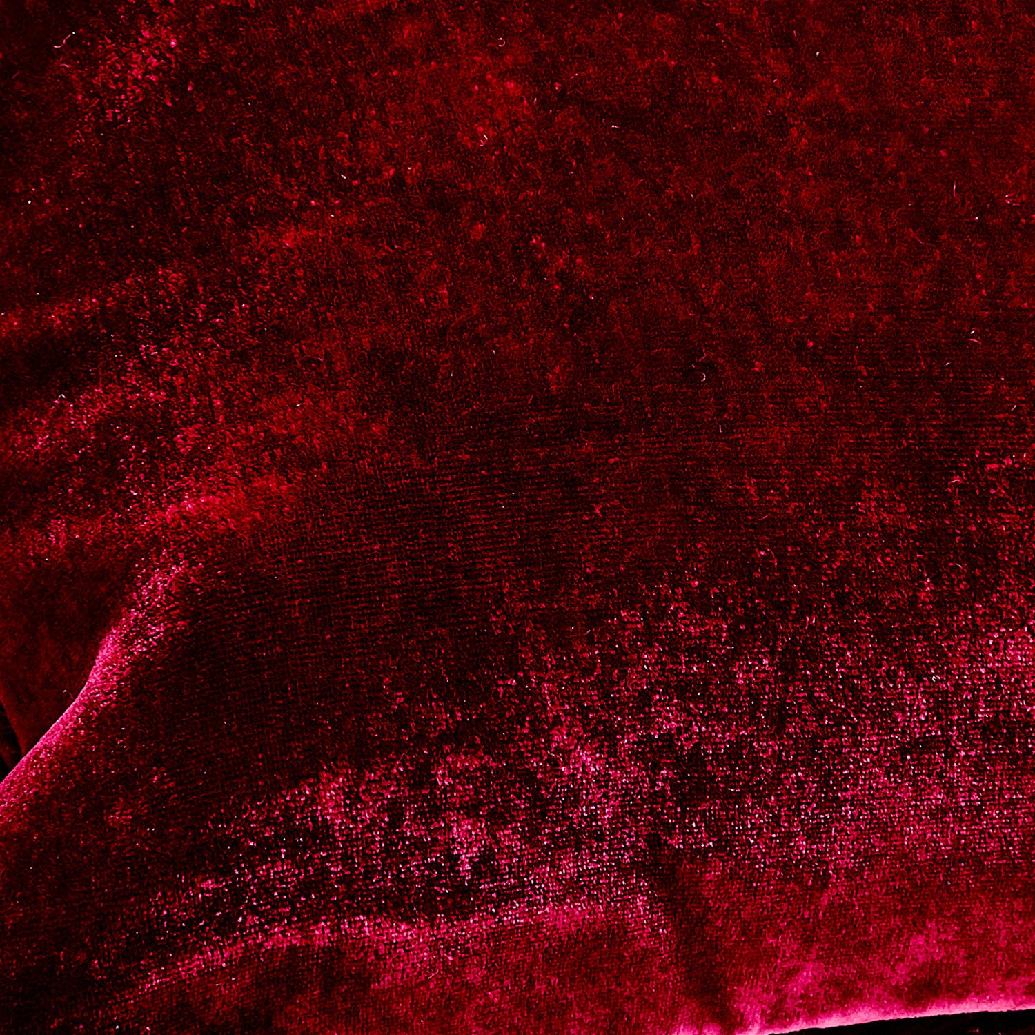 Close-up of vibrant red textured fabric with varying light reflections.