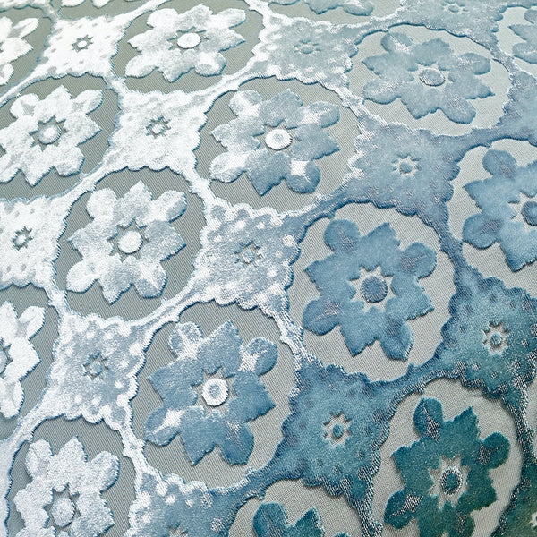 Intricate floral lace fabric in gradient hues of white to blue.