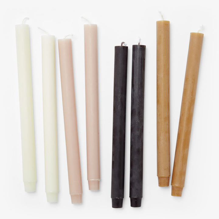 Seven unlit taper candles in various colors arranged horizontally.