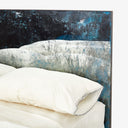 Close-up of a weathered, blue and white headboard with plush bedding.