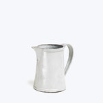 Vintage enamel pitcher with distressed white finish on white background.