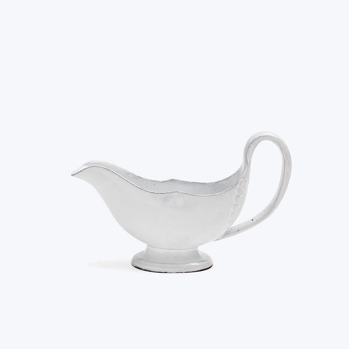 Elegant white gravy boat on pedestal, simple background, scalloped design.