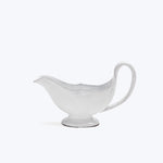 Elegant white gravy boat on pedestal, simple background, scalloped design.