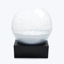 Transparent snow globe filled with sparkling glitter atop black base.
