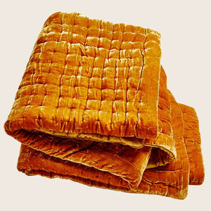 Folded orange velvet quilt with quilted design for ultimate comfort.