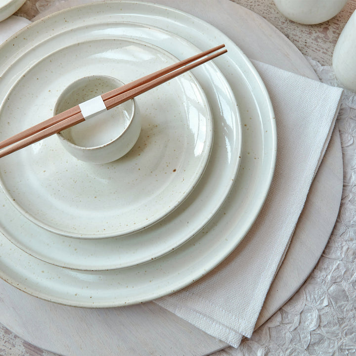 Neatly stacked pastel ceramic tableware with wooden chopsticks on napkin.