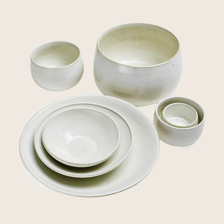 Modern minimalist ceramic dinnerware set with speckled pattern on white.