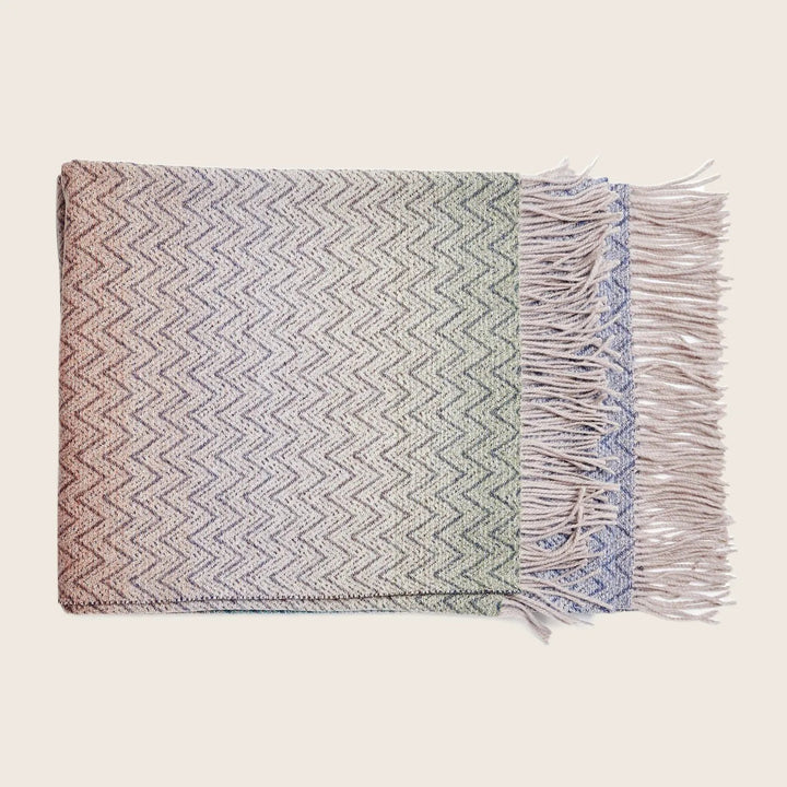 Neatly folded herringbone throw blanket with gradient colors and fringe.