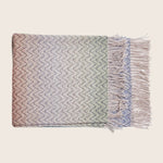 Neatly folded herringbone throw blanket with gradient colors and fringe.
