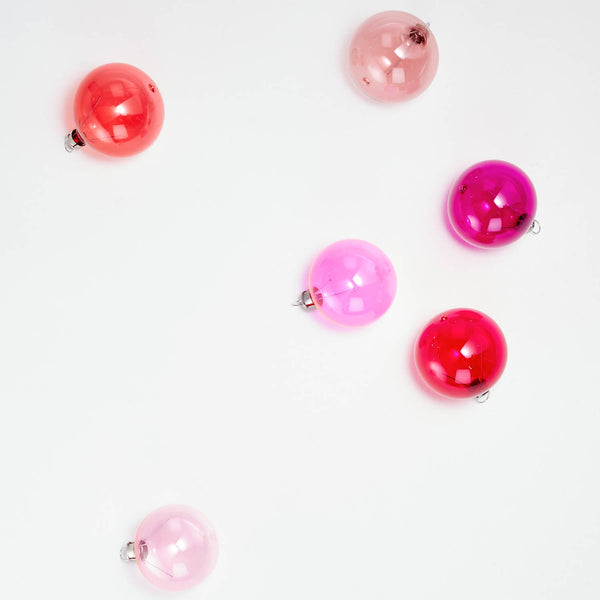 Six glossy, round Christmas ornaments in shades of pink and red.