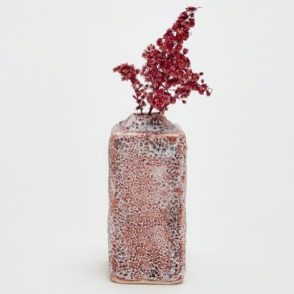 A rustic, weathered vase with textured surface holds dried flowers.
