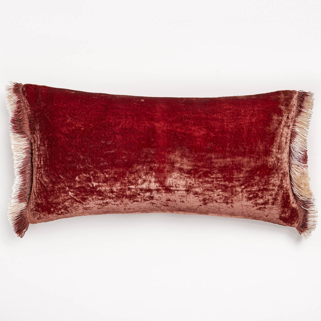 Rectangular red velvet cushion with fringe edges on white background.