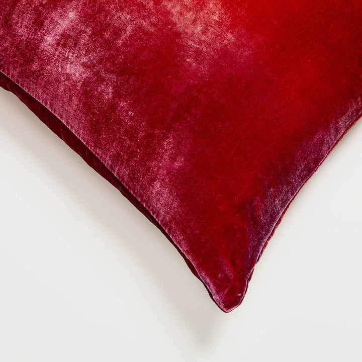 Close-up of plush velvet fabric with gradient from light pink to deep red, showcasing luxurious texture and color variation.
