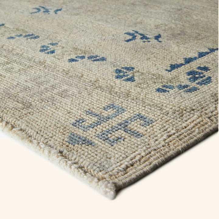 Textured woven rug with traditional blue motifs in bright environment.