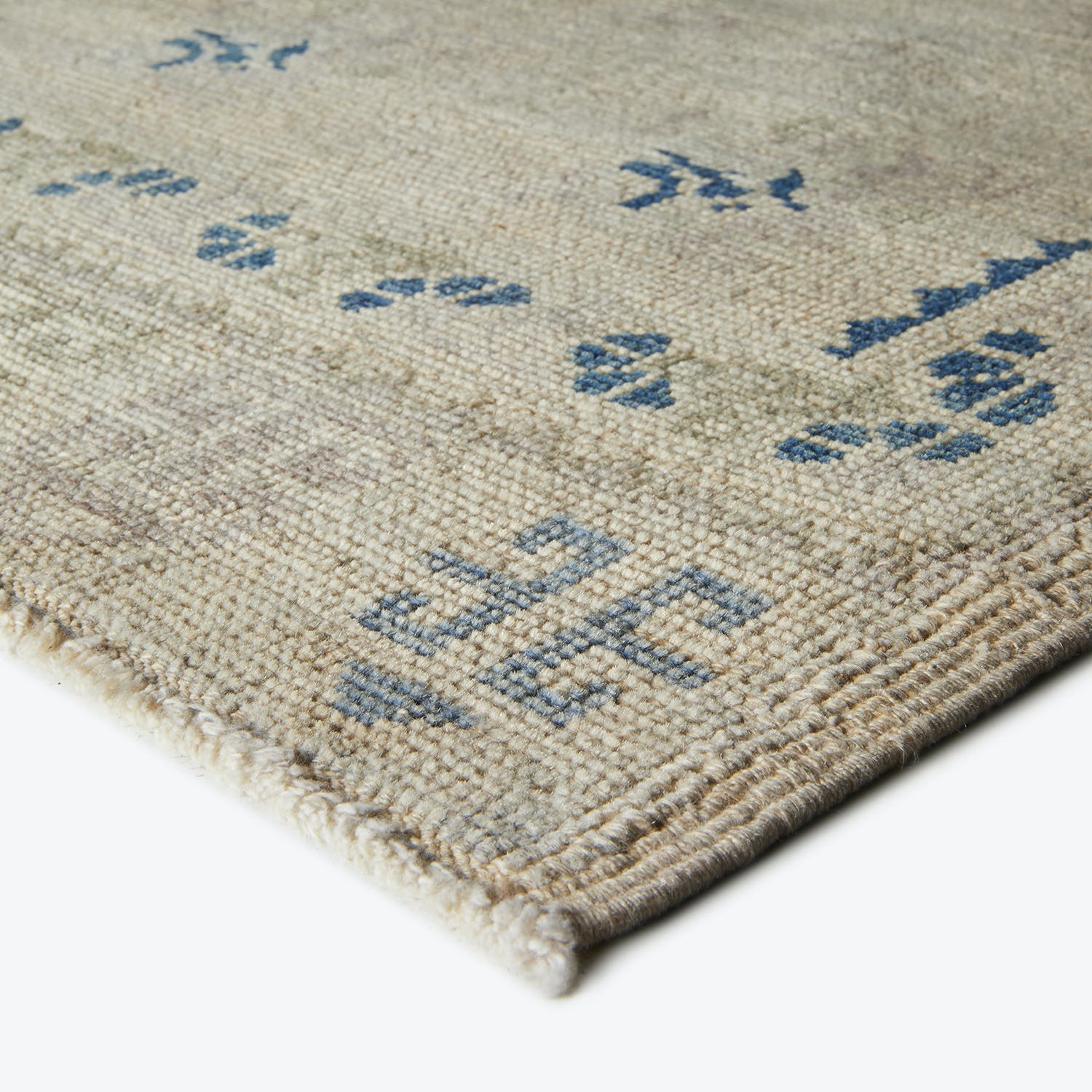 Textured woven rug with traditional blue motifs in bright environment.