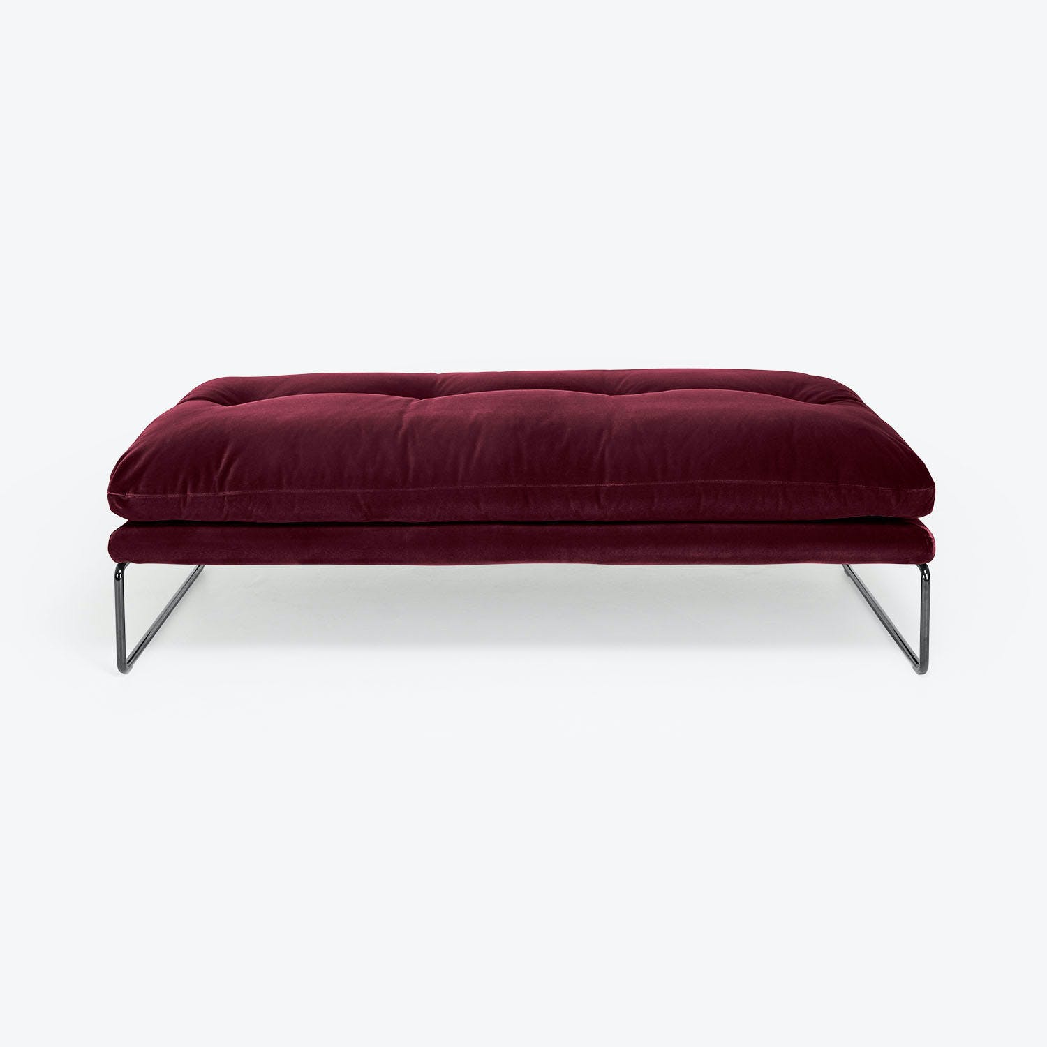 Contemporary burgundy ottoman with plush tufted cushion and sleek metal legs.