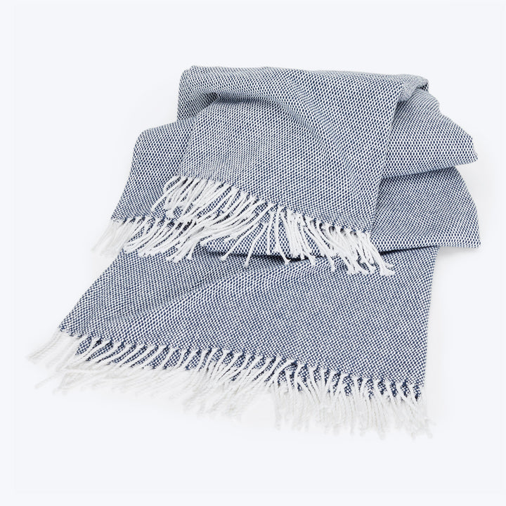 Neatly folded blue and white throw blanket with fringed edges.