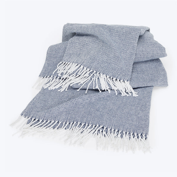 Neatly folded blue and white throw blanket with fringed edges.