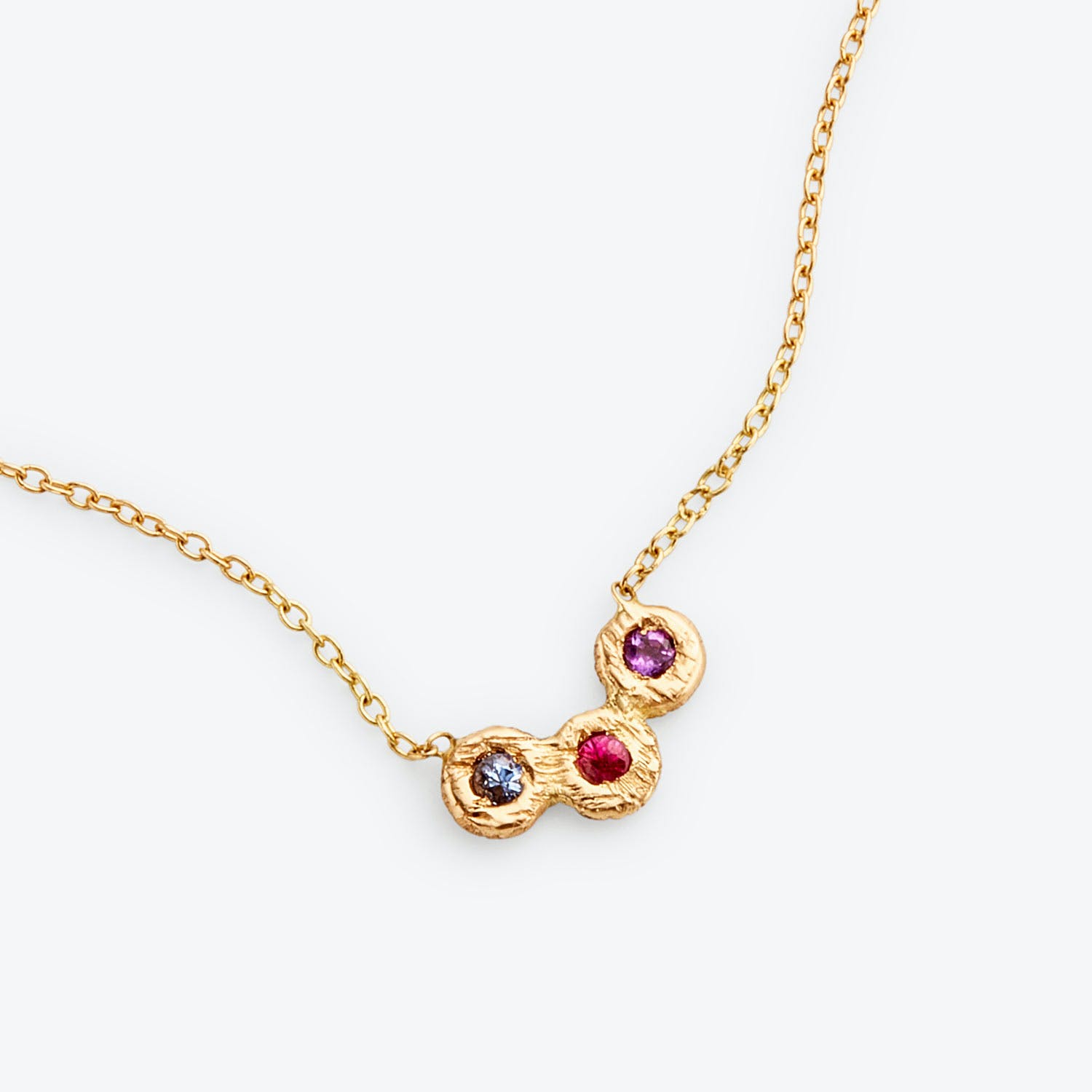 Delicate gold necklace with textured pendant and colorful gemstones.