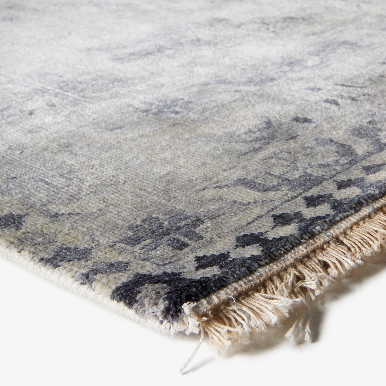Close-up of a grey rug with navy/black motifs and fringed edges.