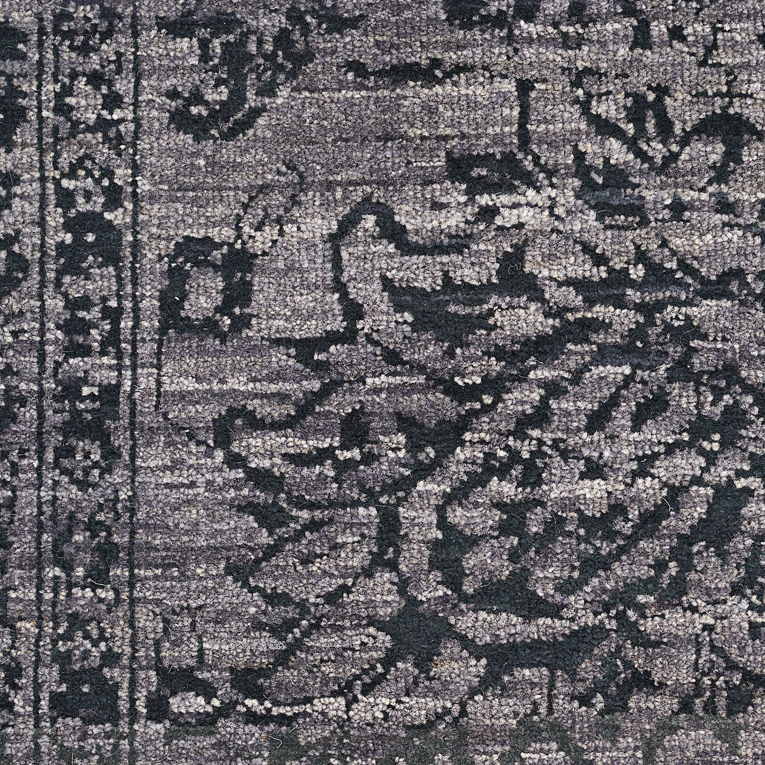 Close-up of a gray rug with ornate floral pattern and texture.